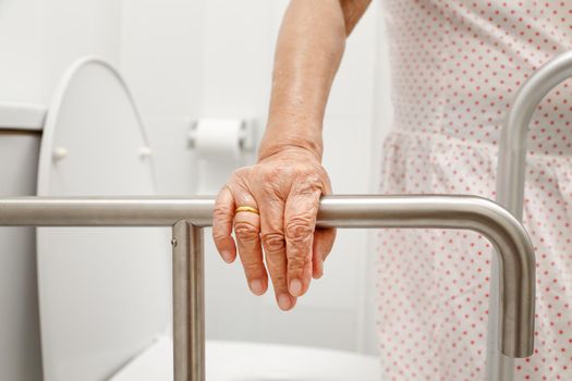 Elderly woman holding on handrail in toilet.