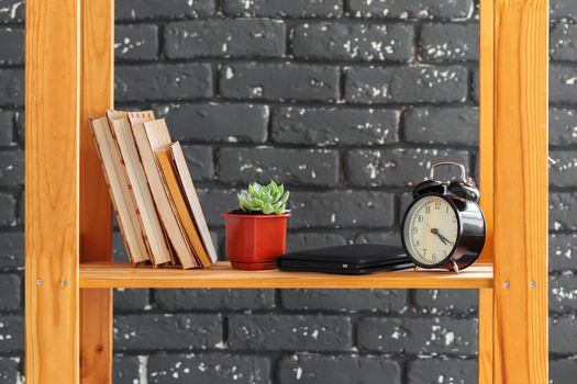 Wooden bookshelf with books and stuff against black brick wall. Close up.