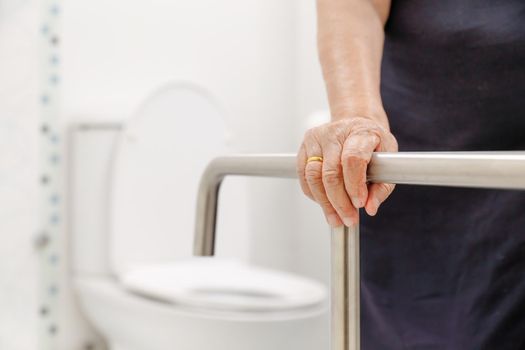 Elderly woman holding on handrail in bathroom.