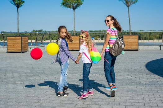 Back view of children schoolgirls holding hands walk together on urban road outdoors background.