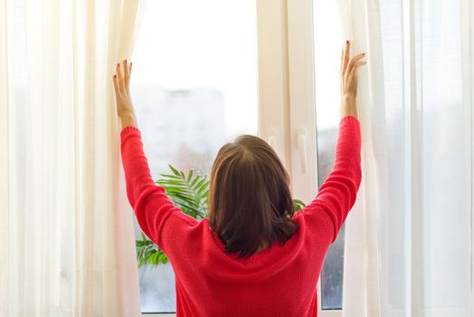 Woman looks out the window, opens the curtains. View from the back