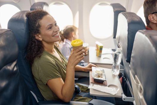 Happy female passenger drinking coffee and smiling while female flight attendant serving lunch on board. Travel, service, transportation, airplane concept