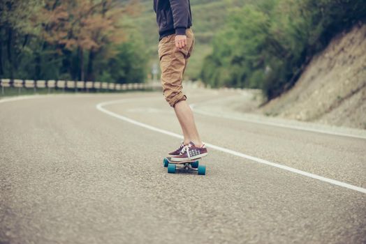 Unrecognizable young man riding on longboard on road in autumn outdoor