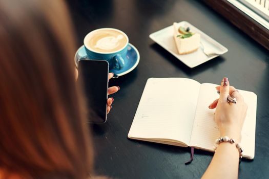 Young business woman sitting at the table in a coffee shop and making notes. Close up.