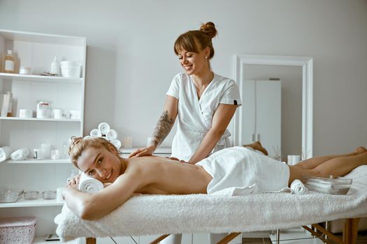 confident female specialist is doing relaxing body massage for beautyful slim caucasian lady at minimalistic spa salon