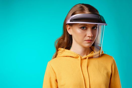 Young woman wearing medical protective face shield against blue background