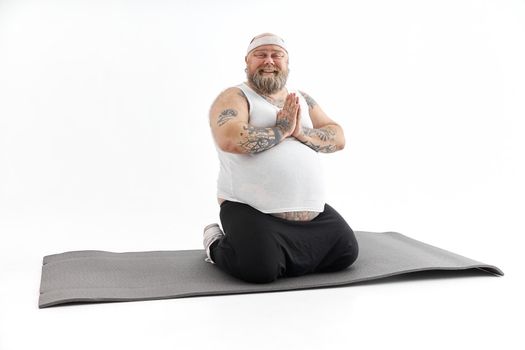 Sporty fat man with beard and tattoos is doing yoga