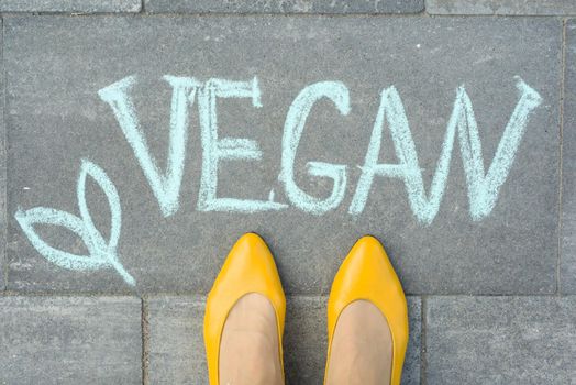 Female feet with text vegan written on grey sidewalk.