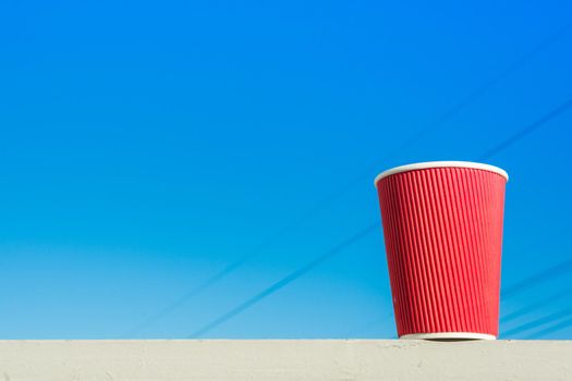 Red paper cup. Blue sky background, copy space