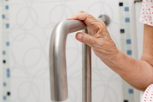 Elderly woman holding on handrail in toilet.