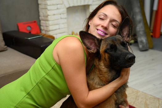 Caucasian woman with a smile hugs Belgian Shepherd dog by the neck in the room at home