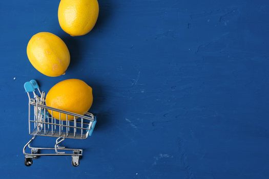 Lemon in shopping cart on classic blue background, top view. Close up.