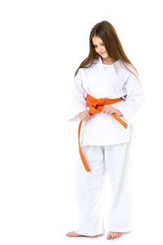 Teenage girl dressed kimono with orange belt. Cheerful beautiful long haired girl dressed sportswear tying her belt on isolated white background. Healthy lifestyle, sport and fitness concept