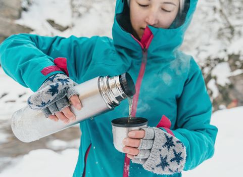 Traveler young woman pouring tea from thermos in winter outdoor