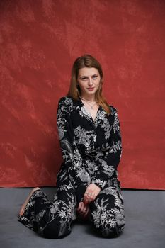 woman in dark clothes sits on the floor on a dark burgundy background