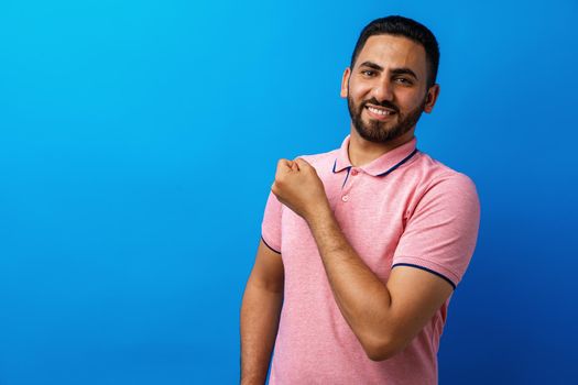 Hispanic man with beard wearing casual t-shirt showing arms muscles against blue background, close up