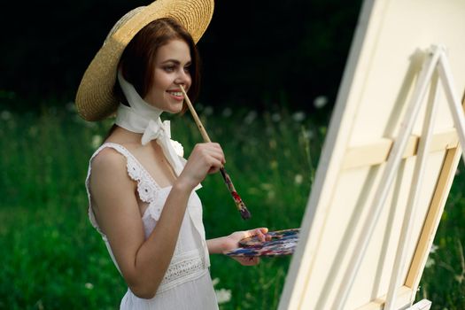 Woman in white dress paints a picture on nature easel. High quality photo