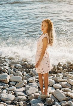 Beautiful young woman walking on pebble coast near the sea, looking at camera.