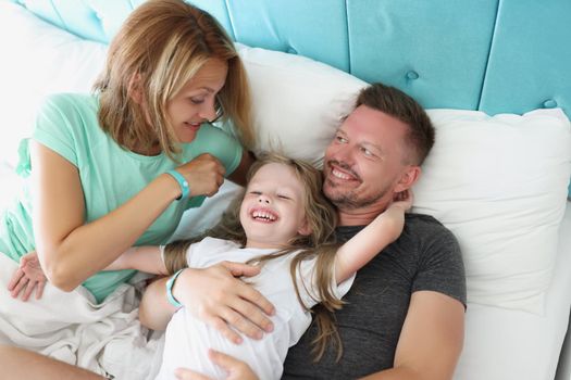 Top view of happy family in bed, father mother and daughter hugging in morning. Start day with family, emotion of happiness. Good morning, family, childhood, parenthood concept