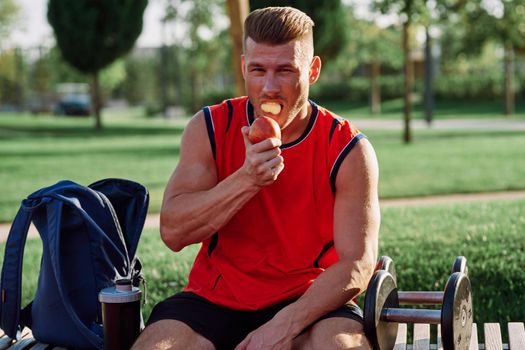 sporty man resting in the park on a bench having a snack. High quality photo