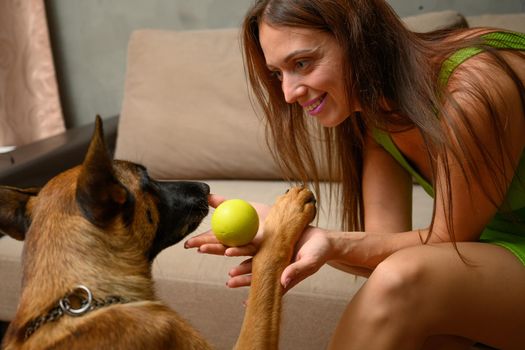 Close-up photo of a girl with a smile sitting on a sofa playing with a ball with a dog at home