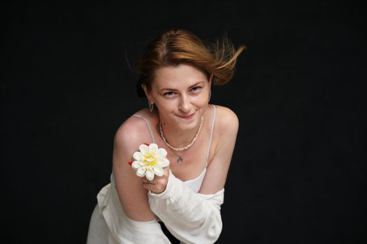 happy model in white shirt posing with flower with smile on black background