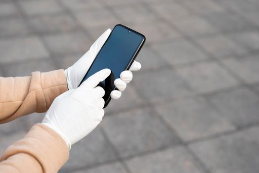Young woman holding a mobile phone in her hands wearing latex protective gloves. Coronavirus spreading precautions measures concept.