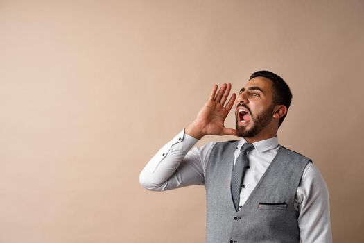 Young arab man shouting and screaming loud against beige background, close up