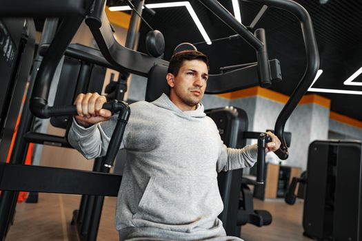 Young fit bodybuilder man doing arms workout training in the gym on machine, close up