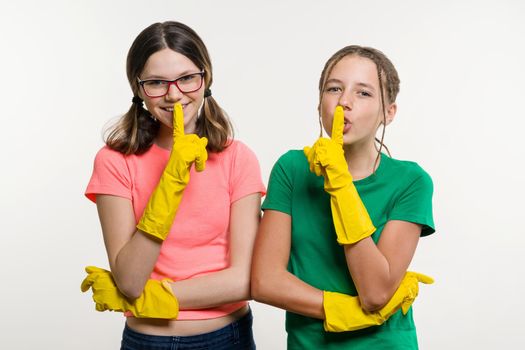 Cleaning, domestic duties and teamwork concept. Two teenage sisters wearing yellow protective gloves show sign quieter, secret.