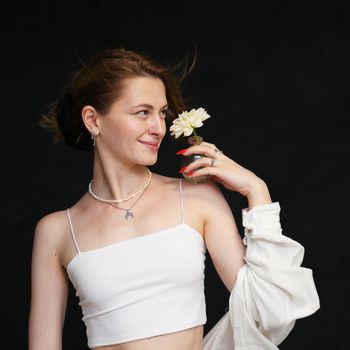 Slim smiling girl in light clothes posing with a flower in the studio on a black background