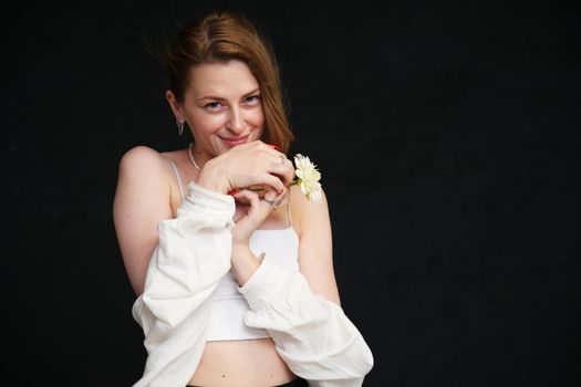 portrait of a cute smiling girl in a white blouse with a flower in her hand in the studio on a black background