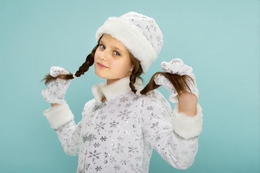 A beautiful girl dressed as a Snow Maiden. Adorable little girl in a white hat and a fur coat embroidered with silver threads, posing in the studio. On Blue Background.New Year and Christmas, Winter Holidays Celebration Concept