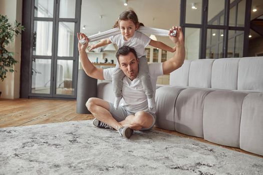 Low angle full length portrait of happy little girl on dad shoulders while they are having fun in living room