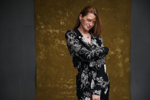 glamorous photo of a caucasian girl in dark clothes posing in a studio on a golden gray background