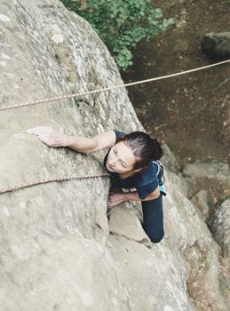 Sporty young woman in safety equipment climbing on rock wall outdoor, top view.
