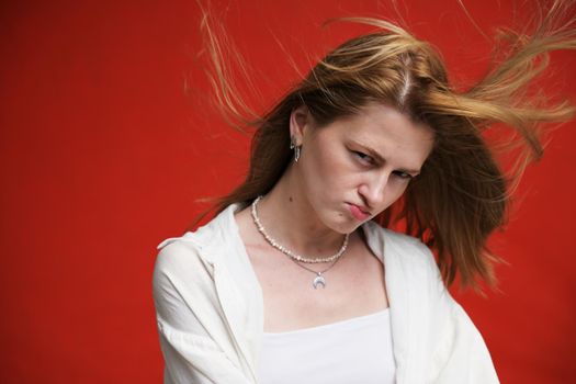 face portrait of a displeased caucasian girl in light clothes on a red background