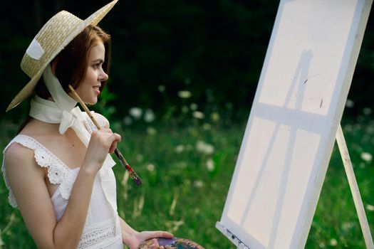 Woman in white dress paints a picture on nature easel. High quality photo