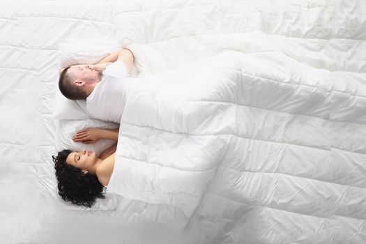 Top view of wife and husband peacefully sleeping on bed, white bedclothes. Wake up and start new day, good morning, every day routine. Good night, comfort, relaxation, family concept