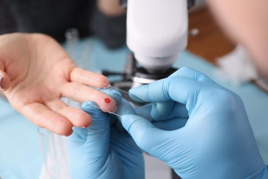 Close-up of medical worker draw blood from patients finger, blood test in hospital. Measurement of blood sugar level, worker in gloves, special equipment for procedure. Medicine concept