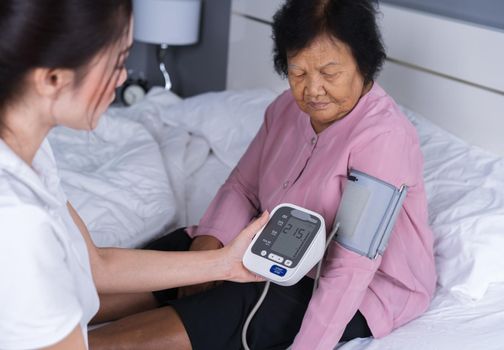 female nurse checking blood pressure of a senior woman on bed