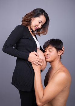young couple: pregnant mother and happy father on gray wall background