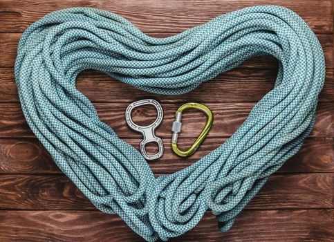 Rope for climbing in the shape of a heart with carbine and figure eight on wooden background, top view.