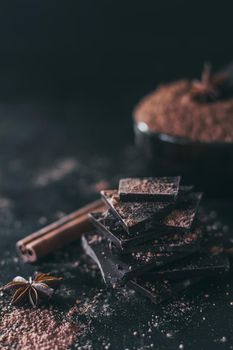 Chocolate bar pieces with cocoa powder on dark background, cope space.