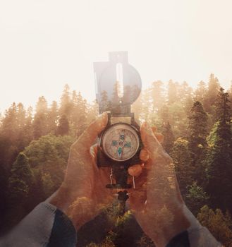 Double exposure image sunset in pine tree forest and female hands with hiking compass.
