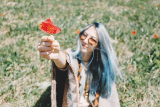 Beautiful young woman with blue hair gives a red tulip outdoor.
