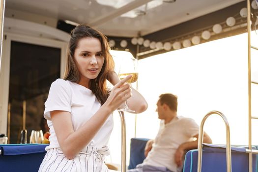 Young woman holding a wineglass and sitting on deck of sailing yacht boat