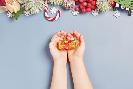 Girl holding a gift on a New Year's background. Children are waiting for gifts ,Christmas tree lights, pine branches, red winter berries and snow. Top view.