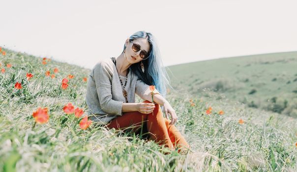 Beautiful young woman in sunglasses rests on red tulip meadow, looking at camera.
