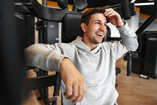 Young fit bodybuilder man doing arms workout training in the gym on machine, close up